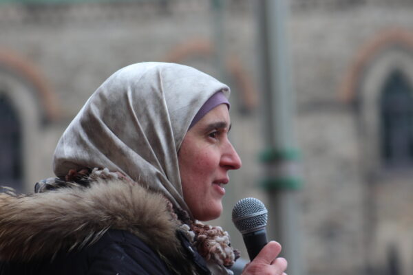 A head covered woman (Maher Arar's Wife) speaks into a microphone at an event in Canada