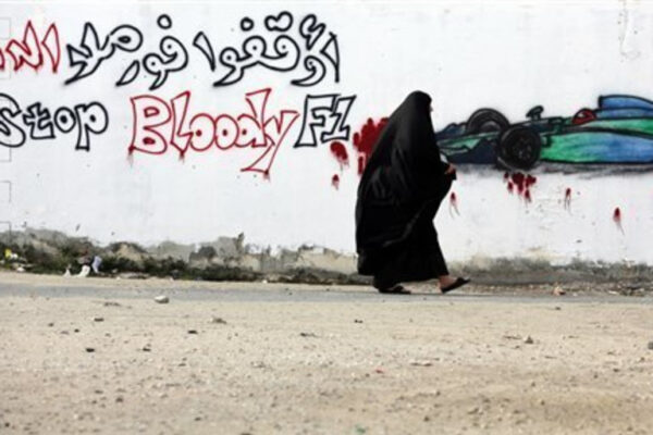 A woman in traditional clothing walks past graffiti that reads 'Stop Bloody F1,'