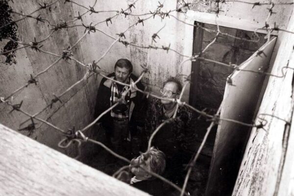 Black and white photo of people standing in a prison cell looking up at barbed wire