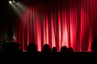 A red curtain with silhouettes of people seated at a theatre