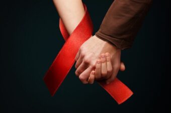 Two hands holding wrapped in a red AIDS awareness ribbon.