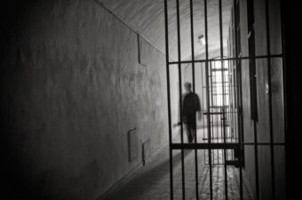 A shadowy figure walking out from what appears to be a jail cell.