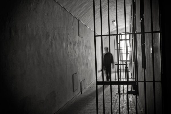 A shadowy figure walking out from what appears to be a jail cell.