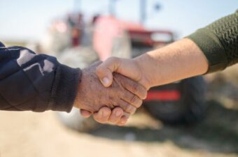 Two farmers' hands shaking, a blurred tractor in the background.