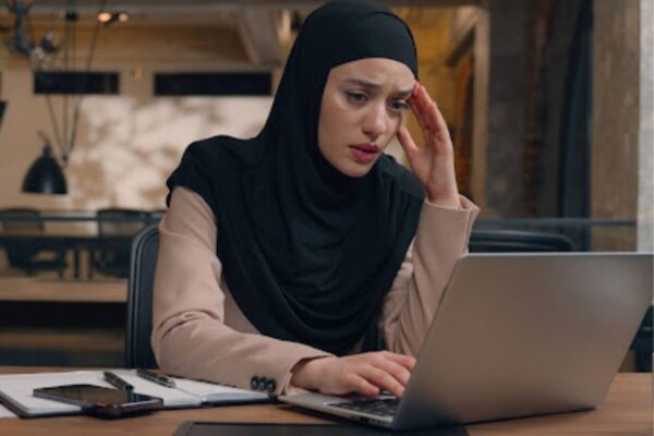 A Muslim woman appears distressed looking at her computer.