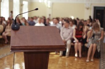 A wooden podium with microphone, a blurred courtroom audience in the background