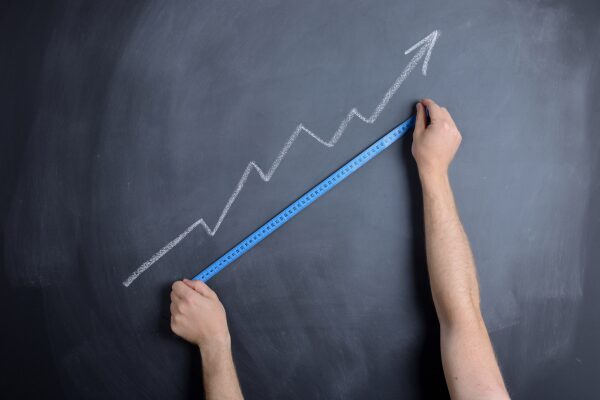 A increasing arrow in chalk on a chalkboard with a measuring tape measuring the growth.