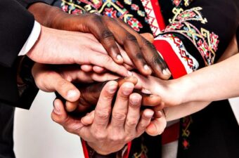 Close-up of diverse hands stacked together in a show of unity and solidarity, symbolizing cooperation and inclusivity across different cultures and backgrounds.