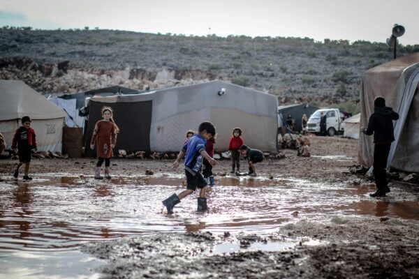 Children in a water and mud flooded refugee camp wearing rubber boots.