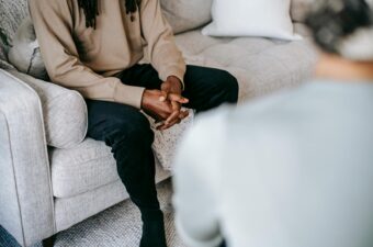 A man sits on a sofa in an office having a conversation with a therapist