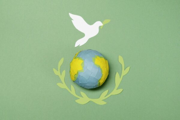 Green background with paper globe and dove cutouts representing peace