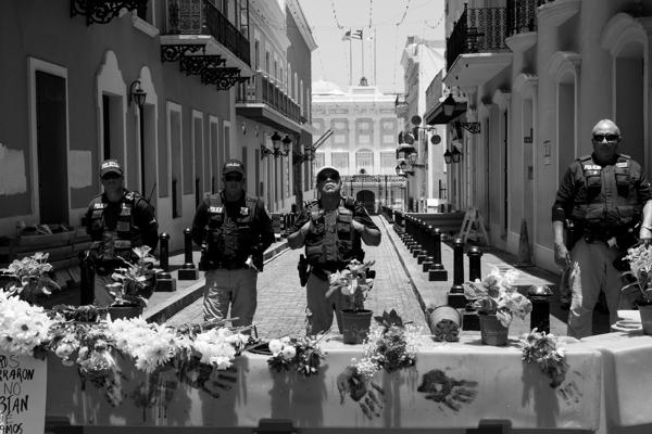 Black and white photograph of law enforcement officers standing in a street with flowers and handprints on a barrier