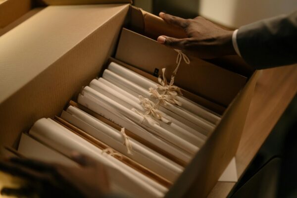 A person's hand on a cardboard box containing many documents for storage.