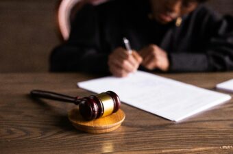 A gavel on a desk and judge in the background appears to be signing a document.