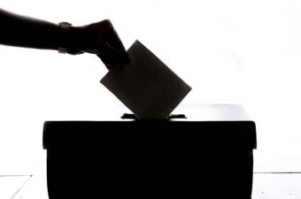 A black and white image of a person dropping a ballot into a box.