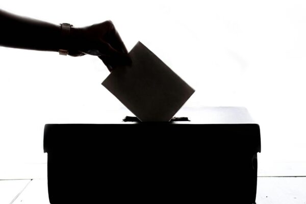 A black and white image of a person dropping a ballot into a box.