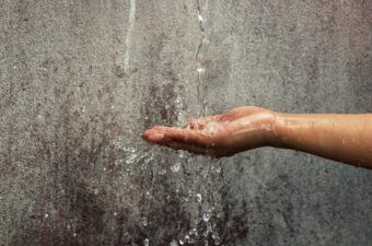 A hand reaches out under running water.