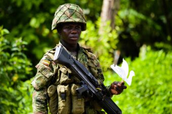 A Colombian soldier in uniform in the jungle, looking sad holding a peace bird cutout