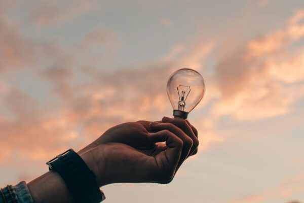 A hand holding a light bulb, a beautiful sky in the background