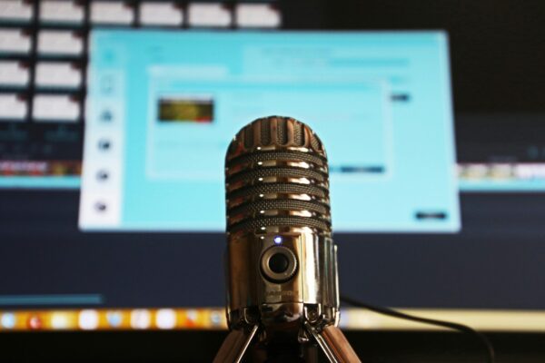 Image of a podcast microphone in front of a computer screen.