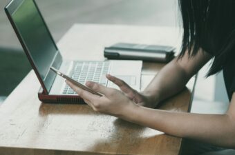 Cropped photo of a girl at a table looking at her phone with her laptop