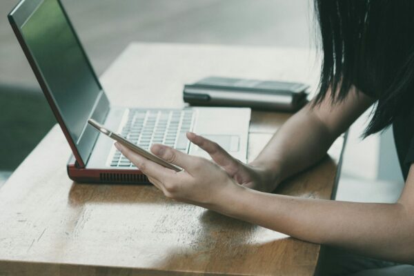 Cropped photo of a girl at a table looking at her phone with her laptop