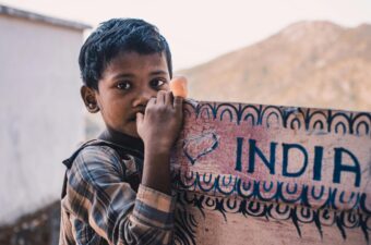 Close-Up Photography Of A Boy Near A Signboard that says India