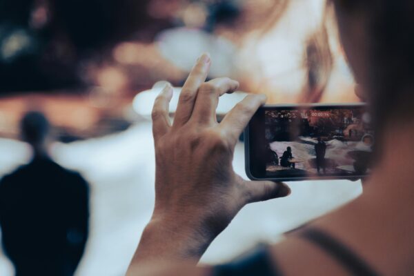 Hands holding a phone horizontally, filming people amongst the snow in the distance.