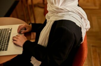 An unidentifiable Muslim woman sits at a computer typing