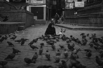 A young Nepali street vendor sits amongst a flock of birds