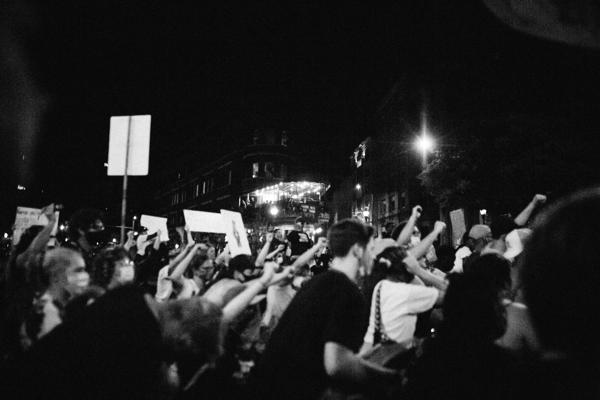 Black and white photo of a nighttime protest with a crowd of people holding signs and raising fists