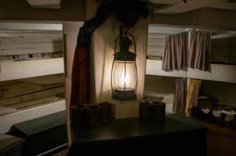 Dimly lit room with a hanging lantern illuminating rustic wooden bunk beds and simple furnishings