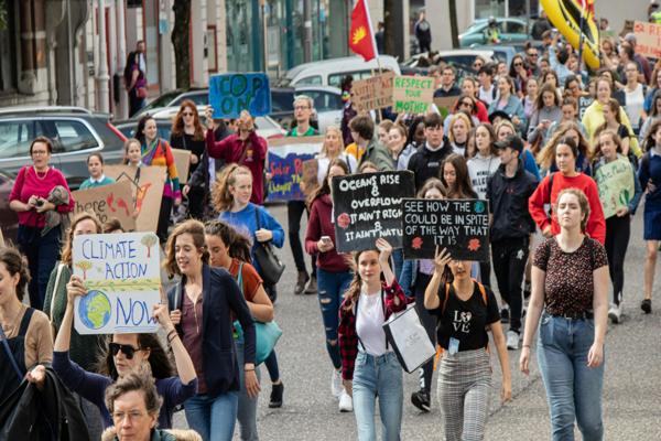 A large group of people marching in a street protest, holding colorful signs advocating for climate action and social justice