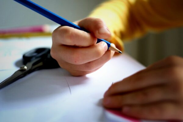 A child's hand holding a pencil and writing on paper.